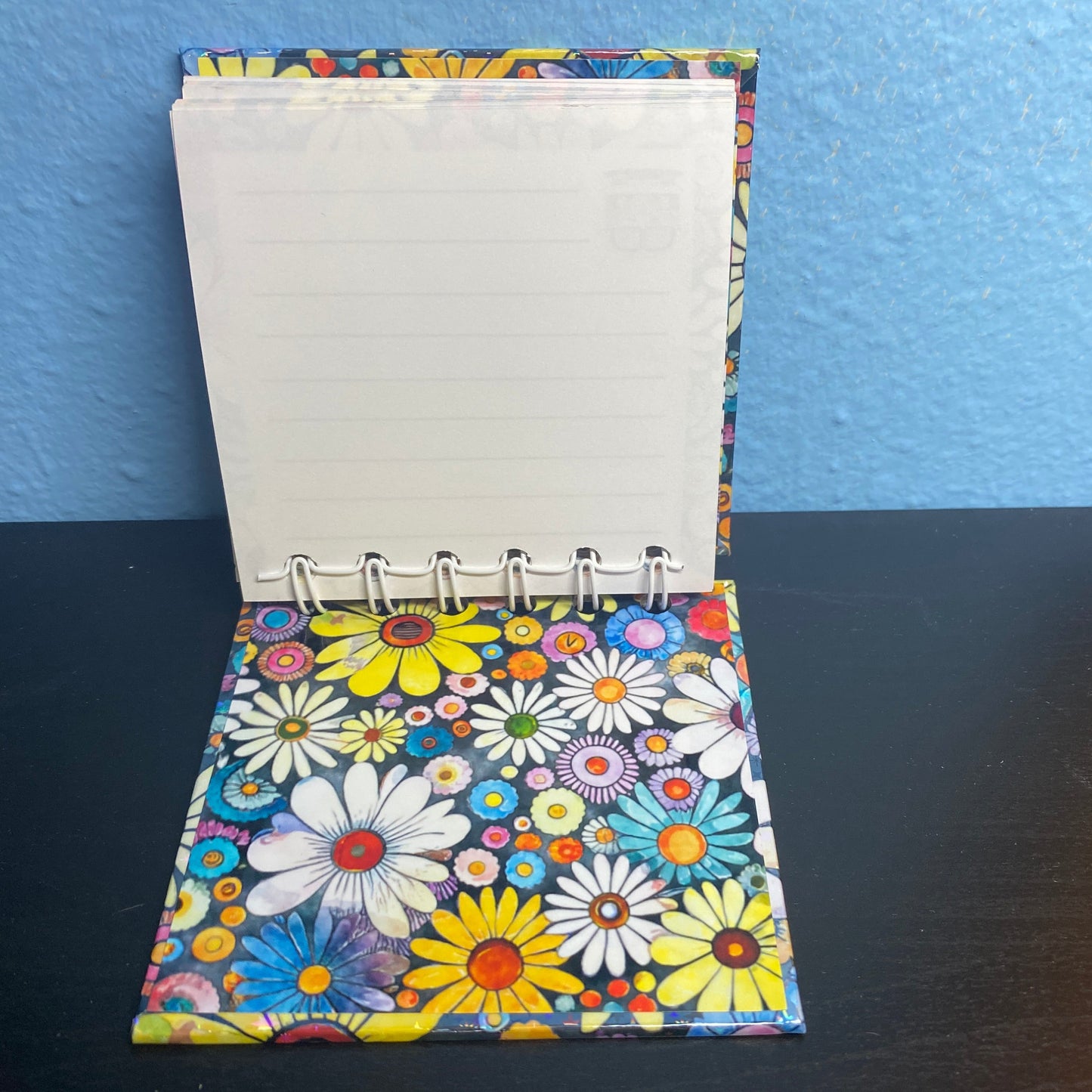 Small notebook with a colorful floral cover on a dark surface.
