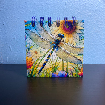 Notebook with dragonfly design on a desk against a white wall