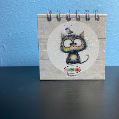 Small notebook with a cat illustration on a dark surface and blue wall background