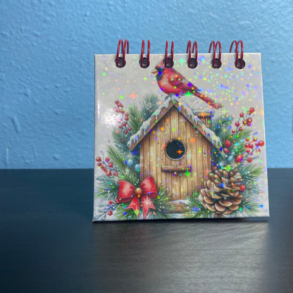 Small calendar with a Christmas-themed design featuring a birdhouse and cardinal on a blue and black background.