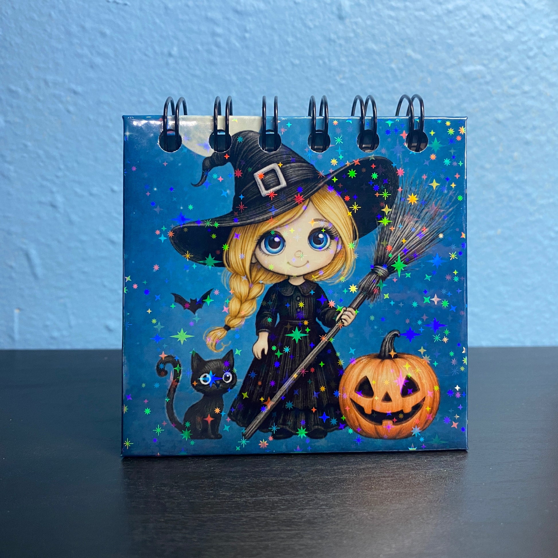 Small notebook with Halloween-themed design featuring a witch, pumpkin, and cat on a blue background.